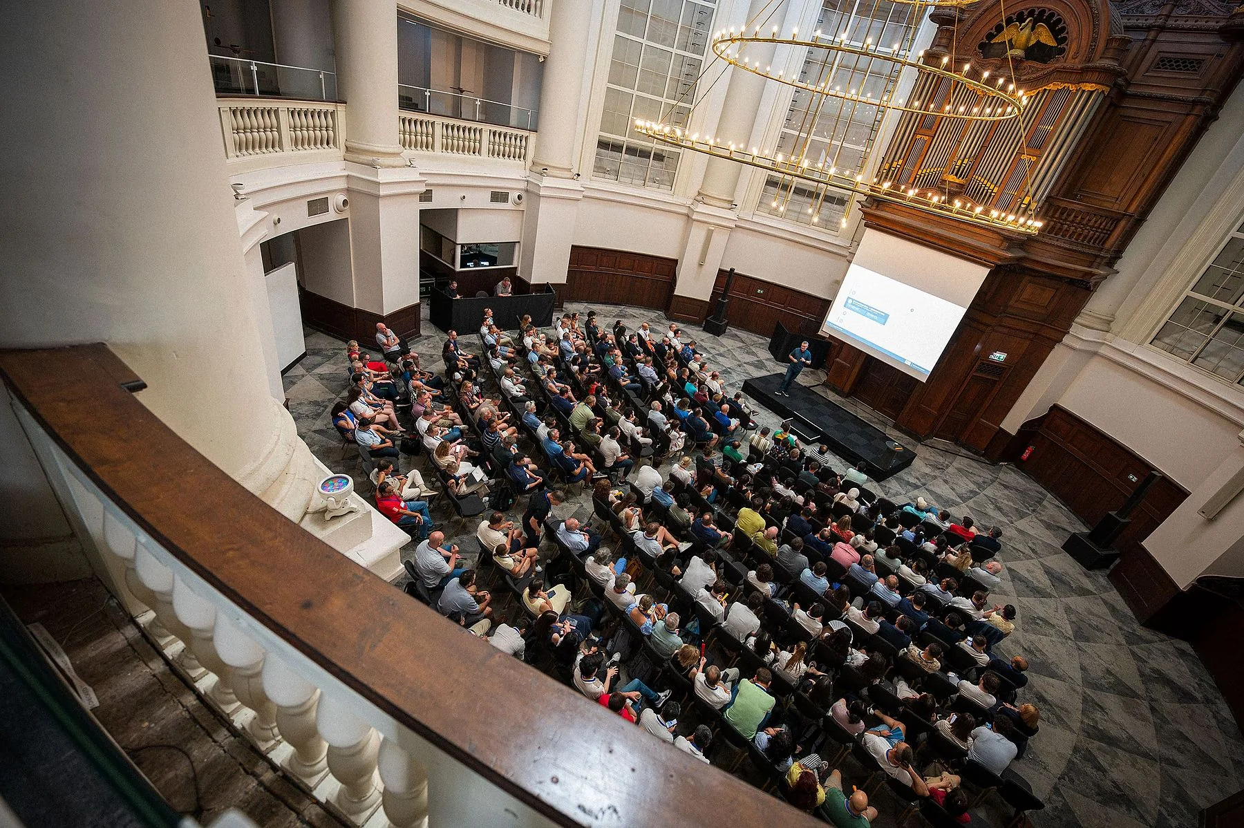 Volle zaal tijdens een congres, gezien vanaf het balkon